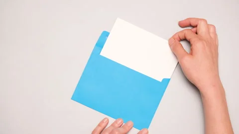 A hand pulls out a white card from a bright blue envelope. Top view of a blue Video stock 271211681