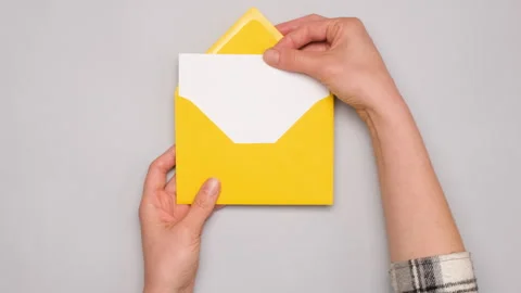 A hand pulls out a white card from a bright yellow envelope. Top view of a Stock Footage 273263230