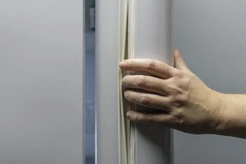 Hand pulls refrigerator door by rubber gasket, demonstrating wrong way to ope Stock Photos