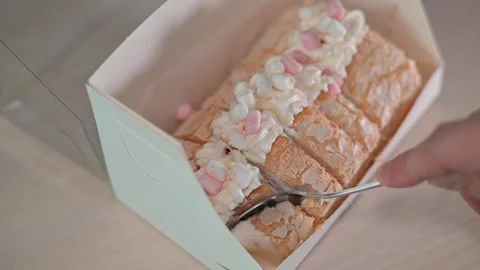 A hand pulls a slice from a dessert box filled with a cream-topped cake Stock-Footage 338188219