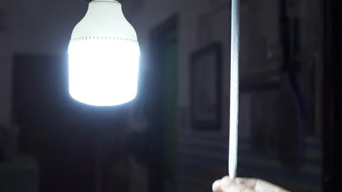 A hand pulls the switch cord and turning on the light in a room at the night Stock Footage 283269141