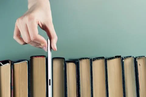 Hand pulls a tablet computer from a row of old paper books, top view Stock-Fotos