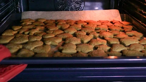 A hand pushes a baking tray out of the oven with Ginger cookies and gingerbread Stock Footage 229152153