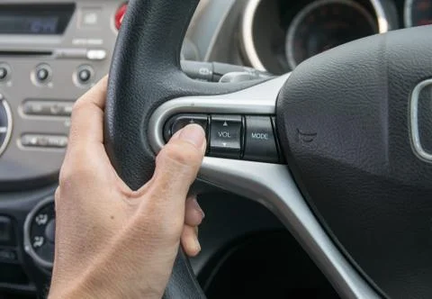 A hand pushes the cruise control button on a steering wheel. Stock Photos