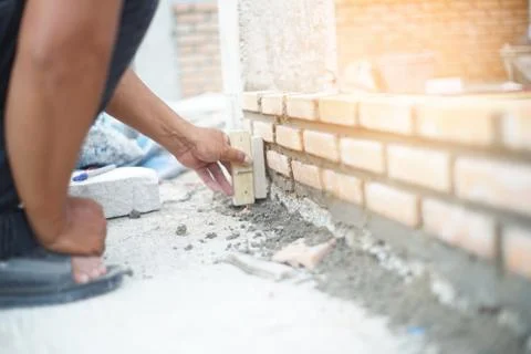 Hand pushes down brick in cement building a wall Stock Photos
