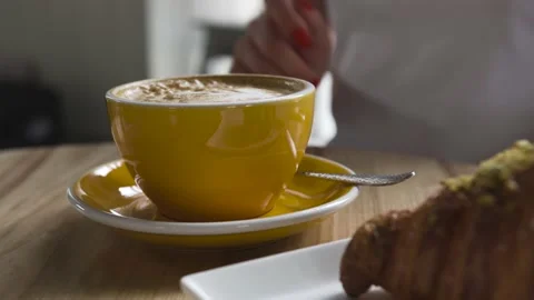 The hand pushes a yellow cup of coffee. Large croissant lies on a plate Stock Footage 137565479