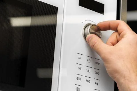 Hand pushing button of microwave oven for cooking food in kitchen Stock Photos