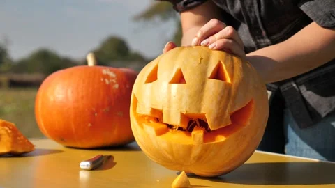 Hand pushing a carved triangular nose out of a pumpkin by carving a pumpkin.. 스톡 동영상 253217627