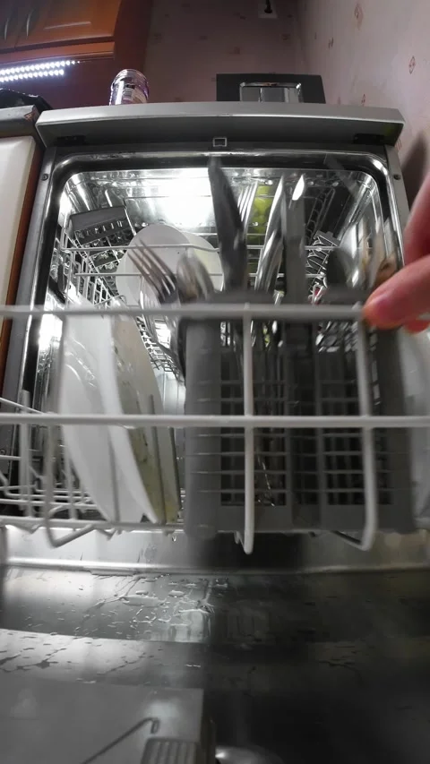 Hand pushing white dish rack into open household dishwasher before wash cycle Stock Footage 325508167