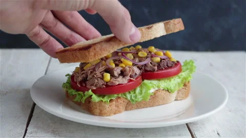 Hand put bbread slice on healthy sandwich with tuna lettuce tomato onion corn Stock Footage 123063763