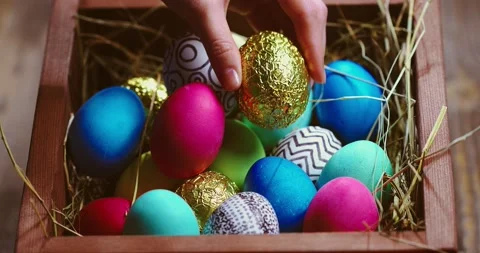 Hand put golden Easter egg on heap of colourful painted eggs on hay in wooden Stock Footage 150952707