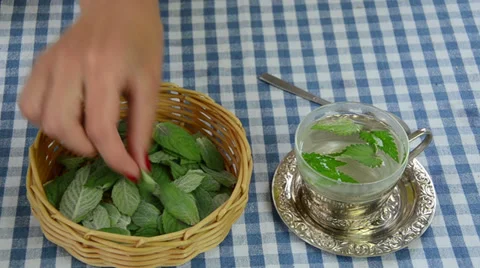 Hand put mint leaves from wicker dish to glass cup with water Stock Footage 33500998