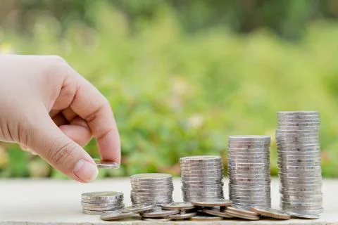 Hand put money coin on stack coins on blurred green natural background. Prope Stock Photos