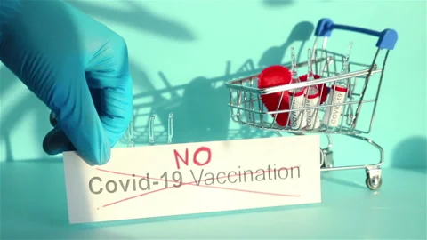 Hand put no covid 19 vaccination sign small shopping cart with vaccine ampoules 스톡 동영상 147537378