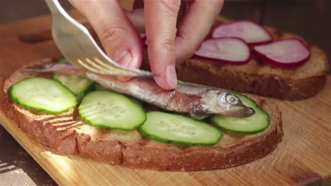Hand put small salted fish sardines capelin on cucumber bread making sandwich Stock Footage 152274697