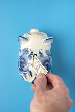 Hand put tiny hundred dollar money into a piggy bank 스톡 사진