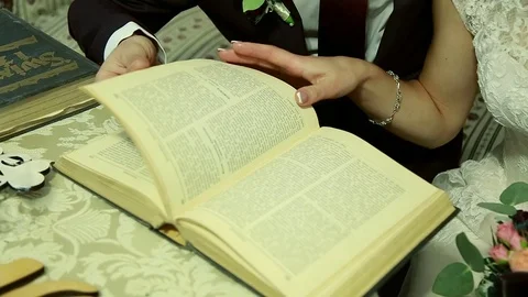 Hand put two wedding rings on a book creating heart shadows Stock Footage 72384332