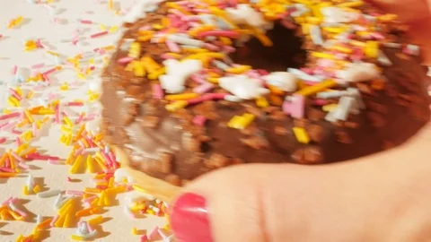Hand puting tasty chocolate donut with sugar rainbow sprinkle on white plate Stock Footage 124461798