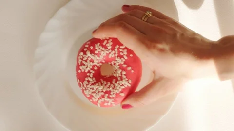 Hand puting tasty red, pink donut with sugar sprinkle on white plate Stock Footage 124461618