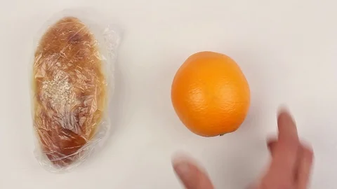Hand puts baked pie in plastic bag to white table, then puts orange, closeup Stockbeeldmateriaal 87596491