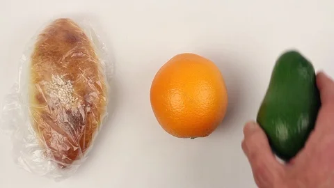Hand puts baked pie in plastic bag to white table, puts orange, avocado, closeup Vídeos de archivo 87596587