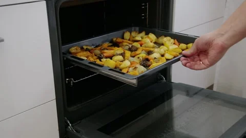 Hand puts baking tray with various roasted vegetables, including potatoes Stock-Footage 329622221