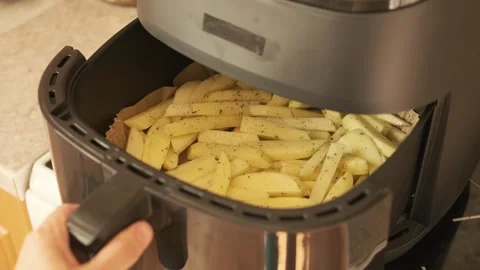 Hand puts basket with raw potato fries into air fryer and presses start button Stock Footage 338273201