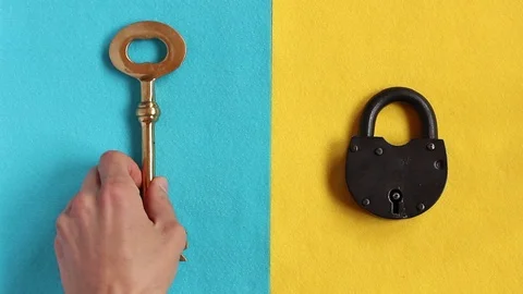 Hand puts black padlock on yellow felt, puts vintage golden key on blue felt Stockbeeldmateriaal 88087264