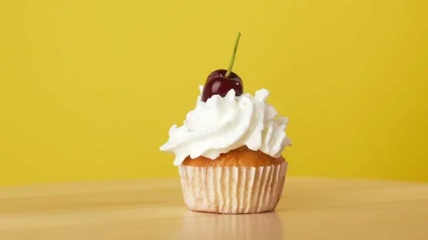 A Hand puts a Cherry on a Cream Cupcake Rotating on a Yellow Background Video stock 202745386