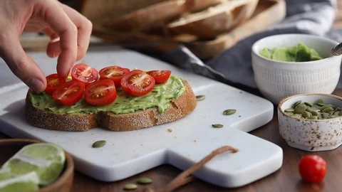 Hand puts cherry tomatoes on an avocado toast. Stock Footage 124329145