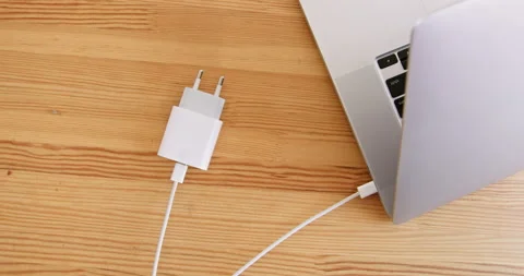 Hand puts cord with plug connected to laptop on table Vídeos de archivo 235433148