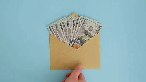Hand puts a craft envelope with dollars from a blue surface, top view Stock Footage 325976683