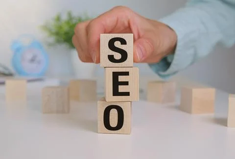Hand puts cubes with SEO text text wooden cube blocks on table background. .. Stock Photos