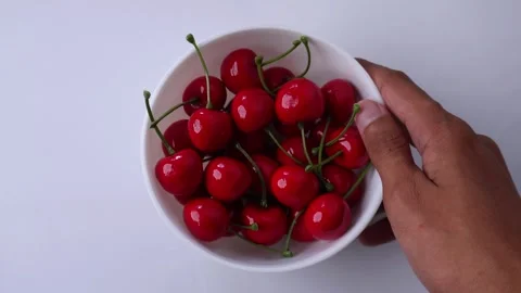 Hand puts down a bowl of cherries on isolated white background Stock Footage 272563177