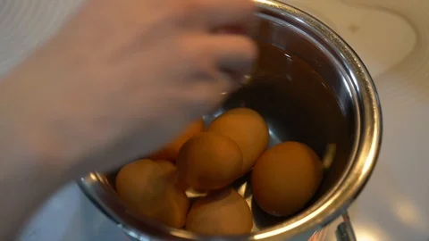 Hand puts eggs in a pan with water to cook Vidéo 88333029