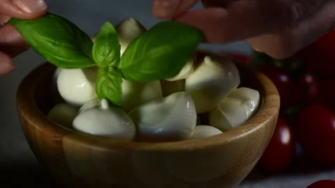 A hand puts the fresh basil leaf on a bowl with mozzarella cheese Stock Footage 153310536