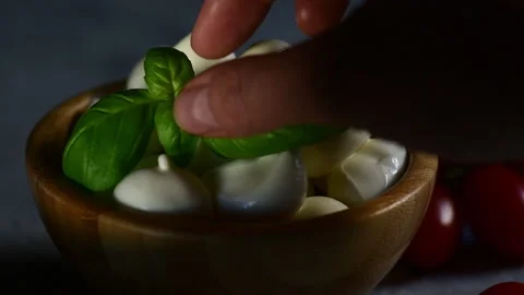 A hand puts the fresh basil leaf on a bowl with mozzarella cheese Stock Footage 153310930