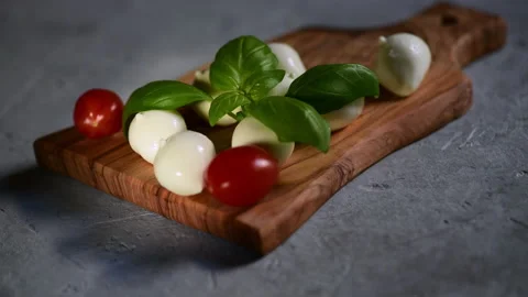 A hand puts the fresh tomatoes on a cutting board with mozzarella cheese Stock Footage 153311405