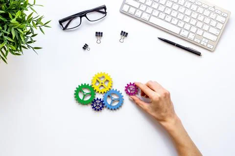 Hand puts a gear into one working mechanism. Teamwork and collaboration concept Stock Photos
