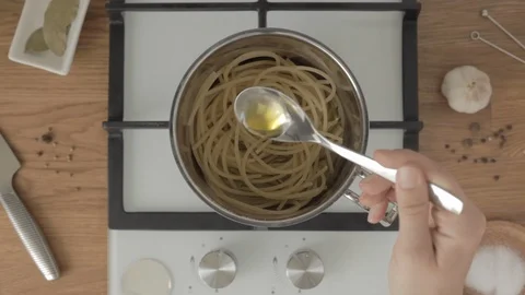 Hand puts half of spoon of oil in metal pan with boiled spaghetti on gas stove 스톡 동영상 114137748