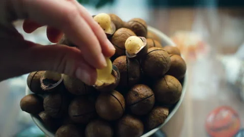 Hand puts the kernel of the macadamia nut. A handful of macadamia in a plate clo Stock Footage 104934887