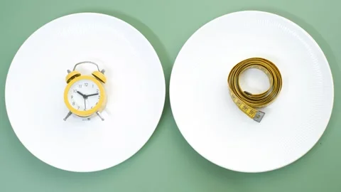 Hand puts measuring tape and alarm clock on  empty plate on green background. Stock Footage 288936778