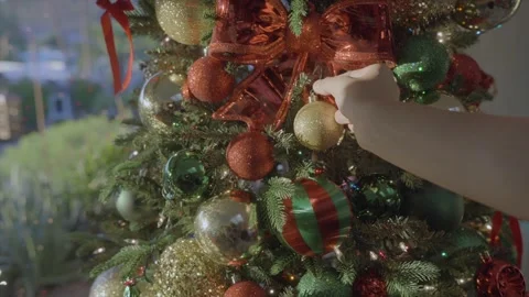 Hand puts ornament on tree window backdrop Видео 348416319