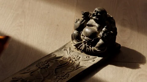 A hand puts a parfumed burning paper in front of a buddha figurine Stock Footage 129759399