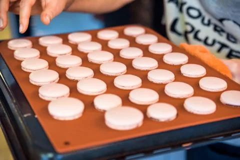 Hand puts pink macroons on baking dish Foto stock