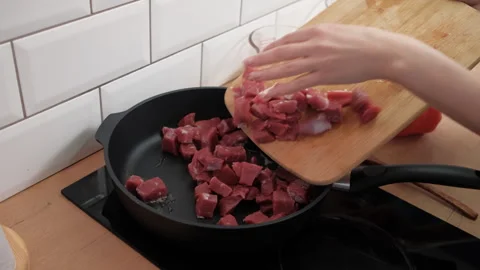 A hand puts red beef meat into a frying pan for cooking. Healthly food Stock Footage 262439294