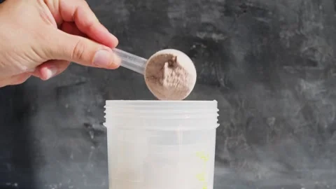 Hand puts into shaker portion of whey protein powder from measuring scoop Stock Footage 251008705