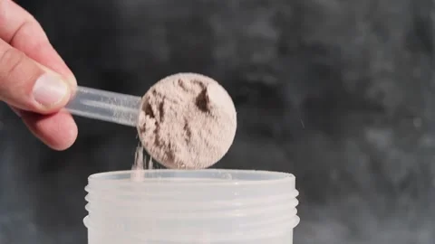 Hand puts into shaker portion of whey protein powder from measuring scoop Stock Footage 251008706