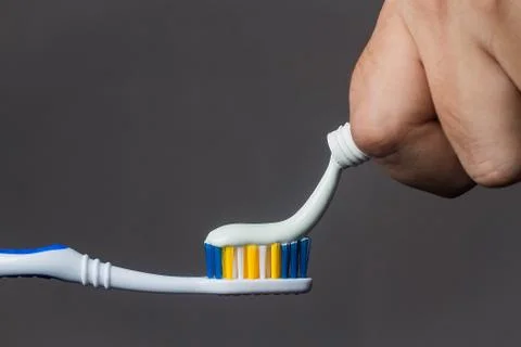 Hand puts toothpaste on the toothbrush on a gray background close-up Stock Photos