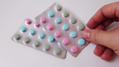 Hand puts two packs of multi-colored pills with vitamins on a white table Video stock 128305779
